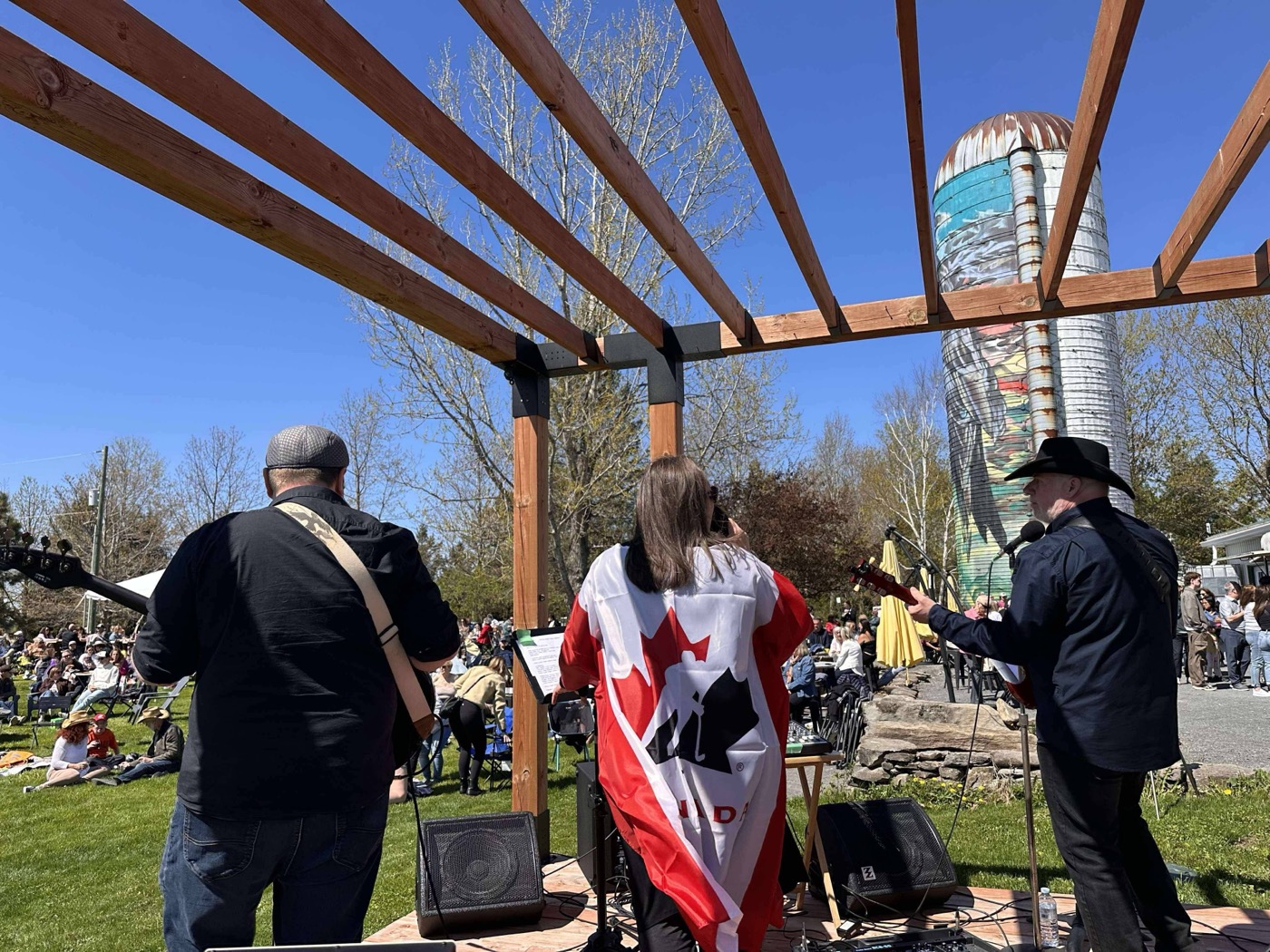The band on stage with a Canadian flag, audience and silo visible beyond the pergola
